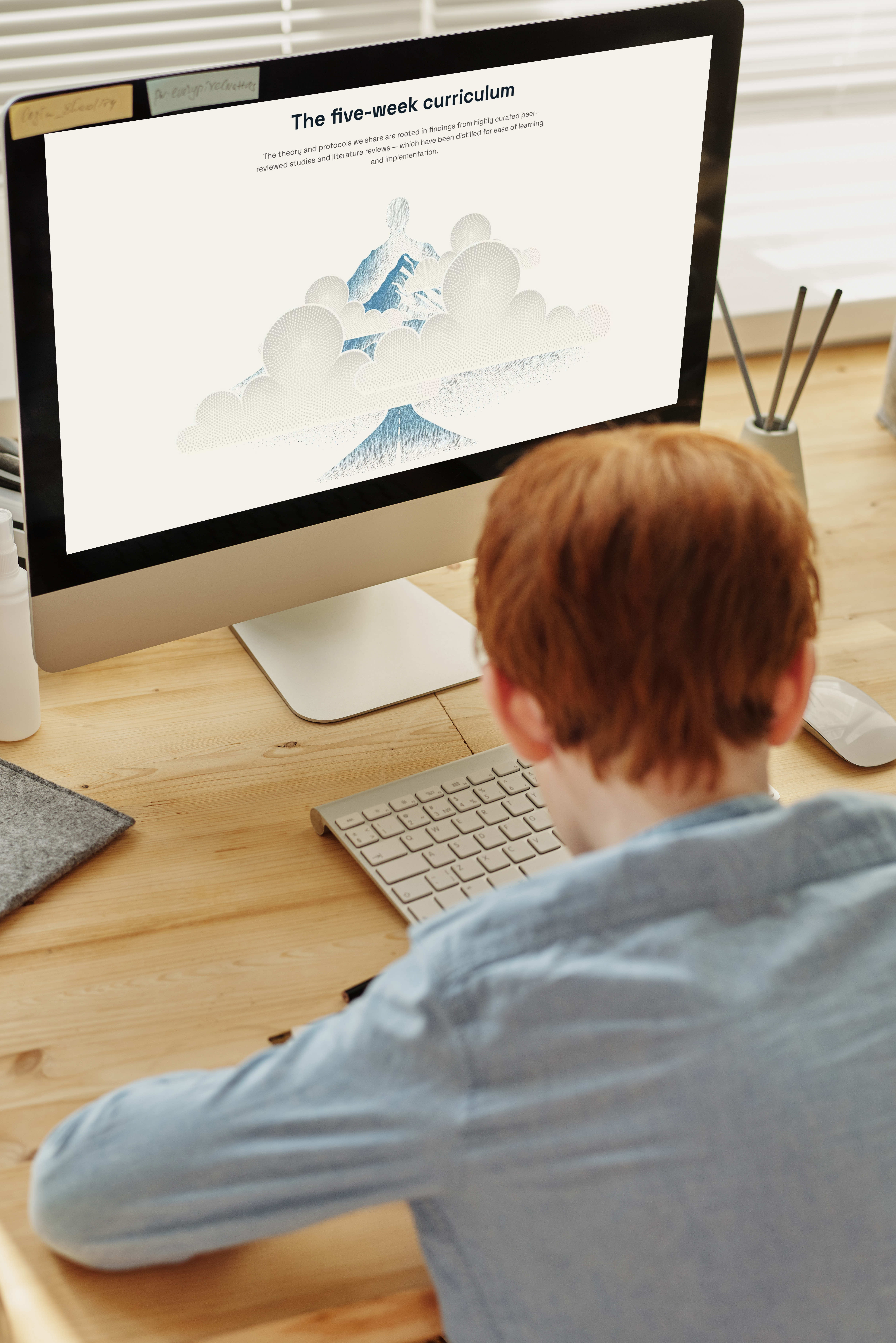 Der Bereich zum fünfwöchigen Lehrplan von Nervous System Mastery auf einem iMac-Bildschirm, aufgenommen über die Schulter eines Kindes am Schreibtisch.